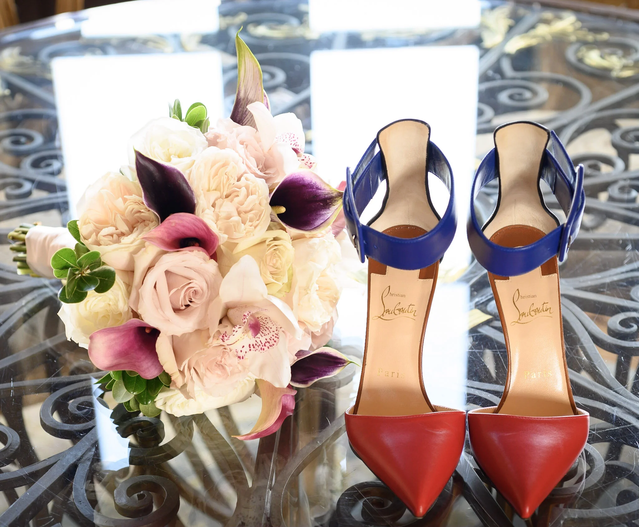 Pair of red high-heeled shoes and a bouquet of pink and white flowers on a glass table.