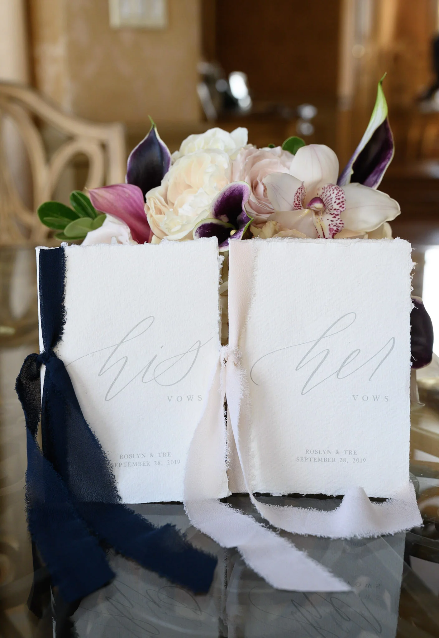 Wedding invitation cards with floral arrangements and ribbons on a reflective surface.