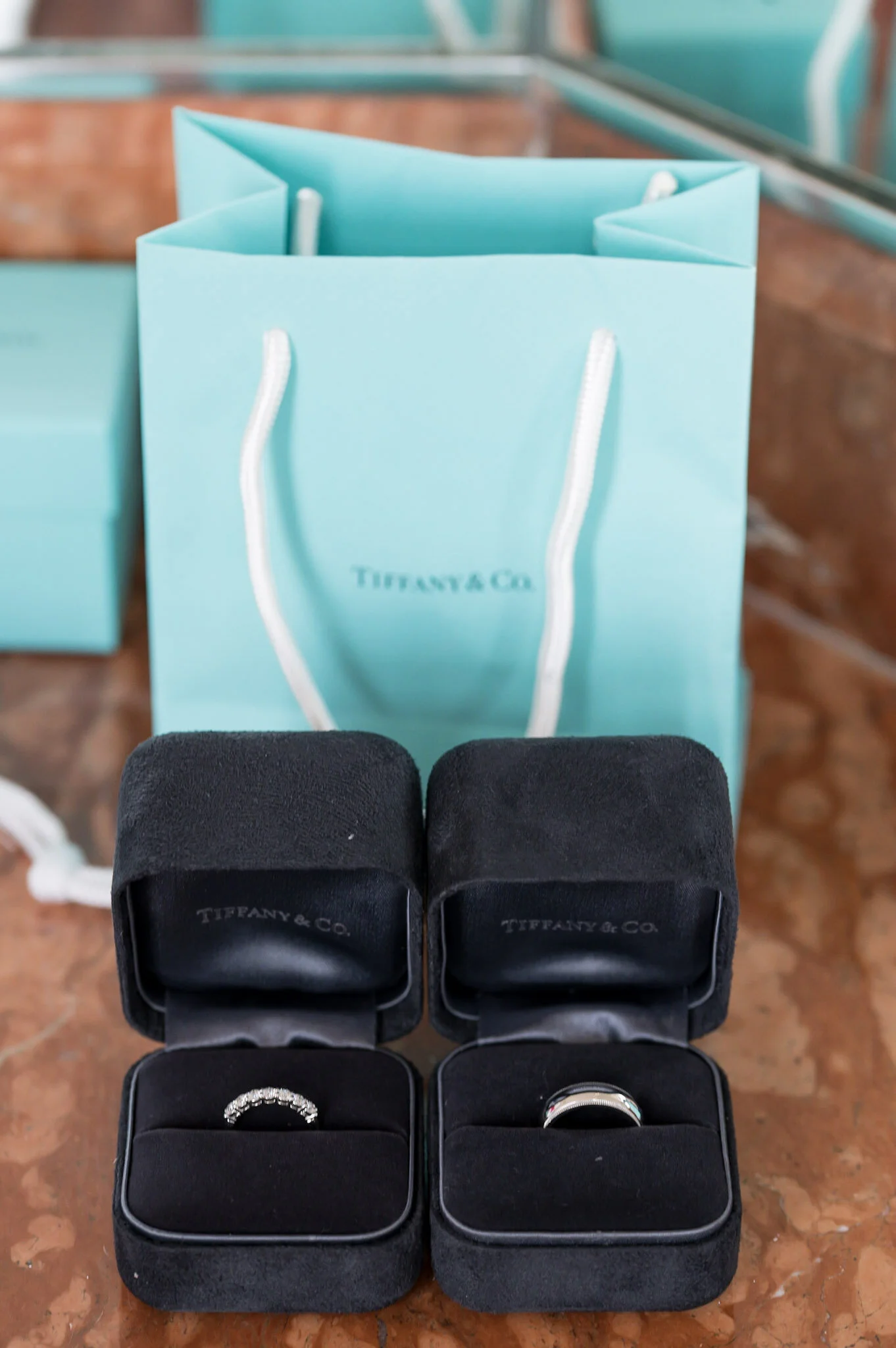 A Tiffany & Co. gift bag behind a display of jewelry boxes with rings.