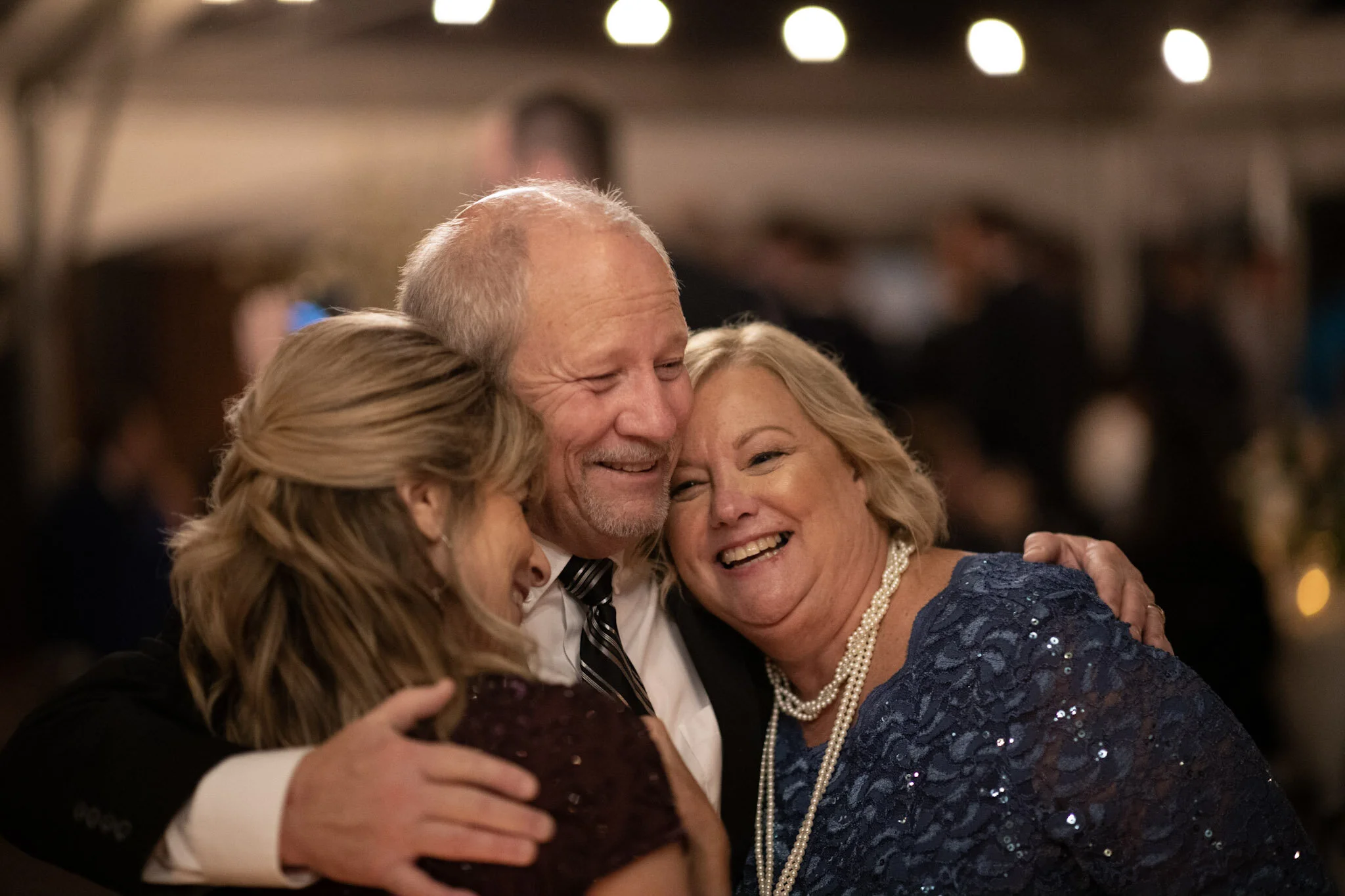 A group of four elderly people embracing and smiling at a celebration or gathering.