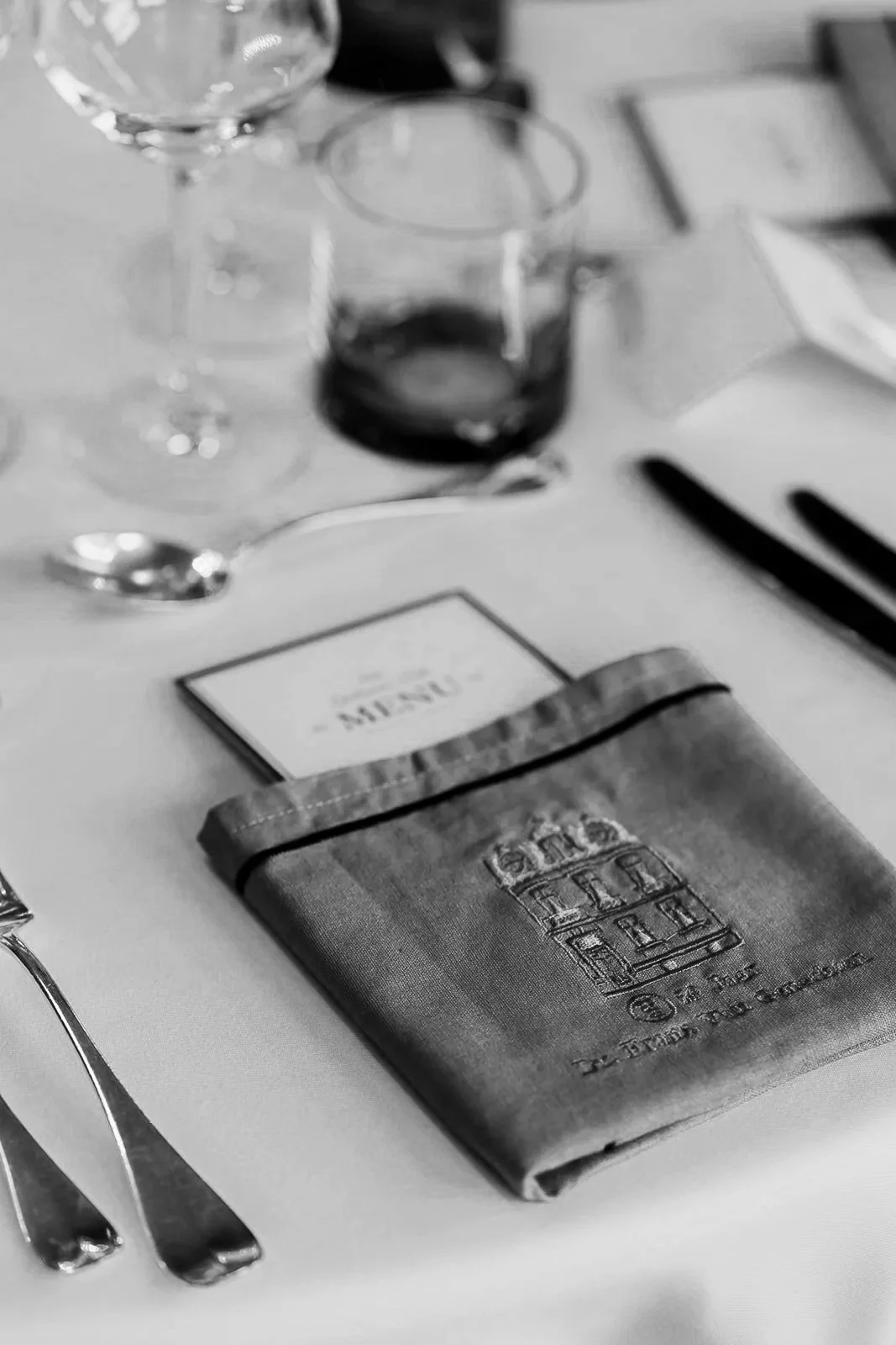 Table setting with wine glasses, a glass of red wine, a black napkin with a building illustration, and a menu.
