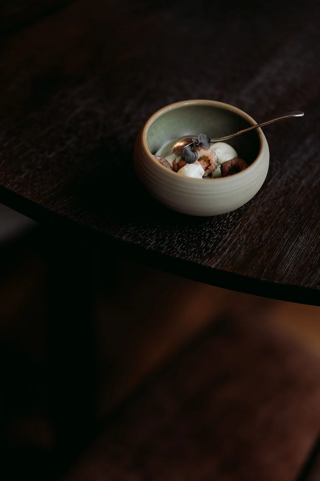 Small ceramic bowl with yogurt, chocolate chips, and nuts on a dark wooden surface.