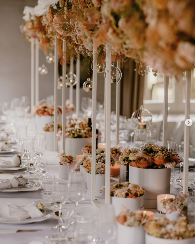 Elegant wedding table decorated with peach and cream floral arrangements, candles, and glass ornaments.