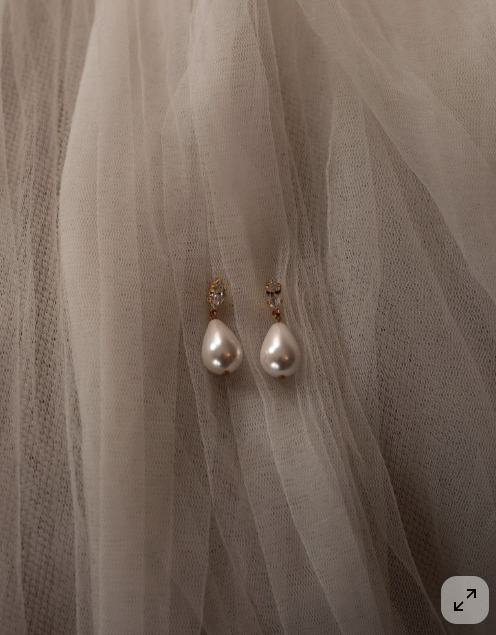 Pearl drop earrings hanging on sheer beige fabric.