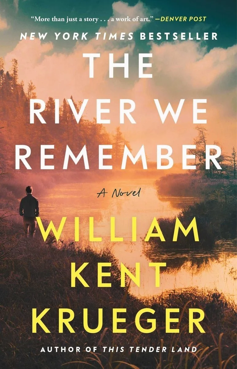 Book cover for 'The River We Remember' by William Kent Krueger, featuring a person standing near a river through a misty, wooded landscape at sunrise or sunset.