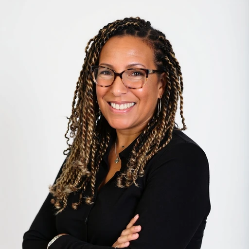 A woman with glasses and braids smiling with arms crossed against a white background.