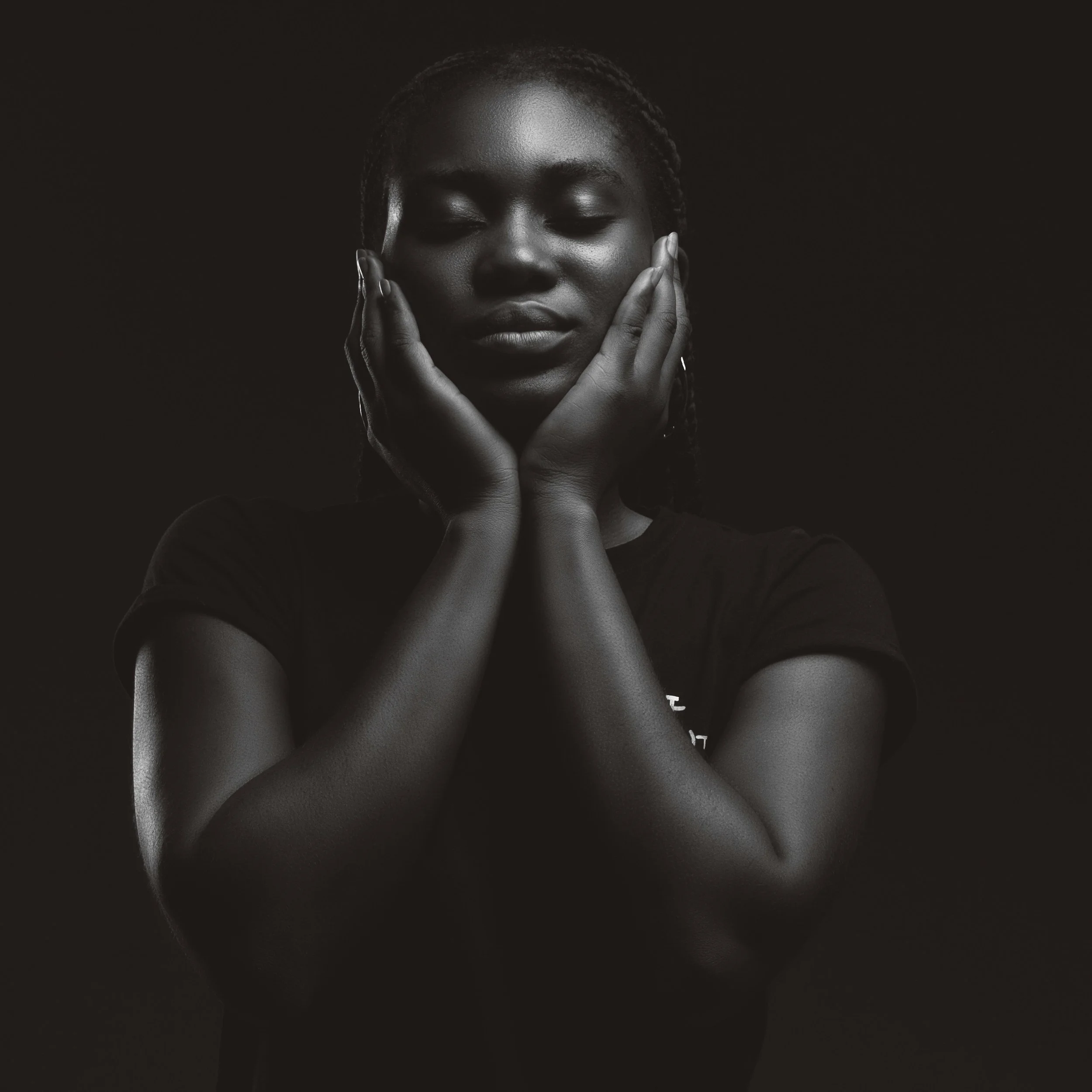 A black and white portrait of a woman with eyes closed and hands gently touching her face.