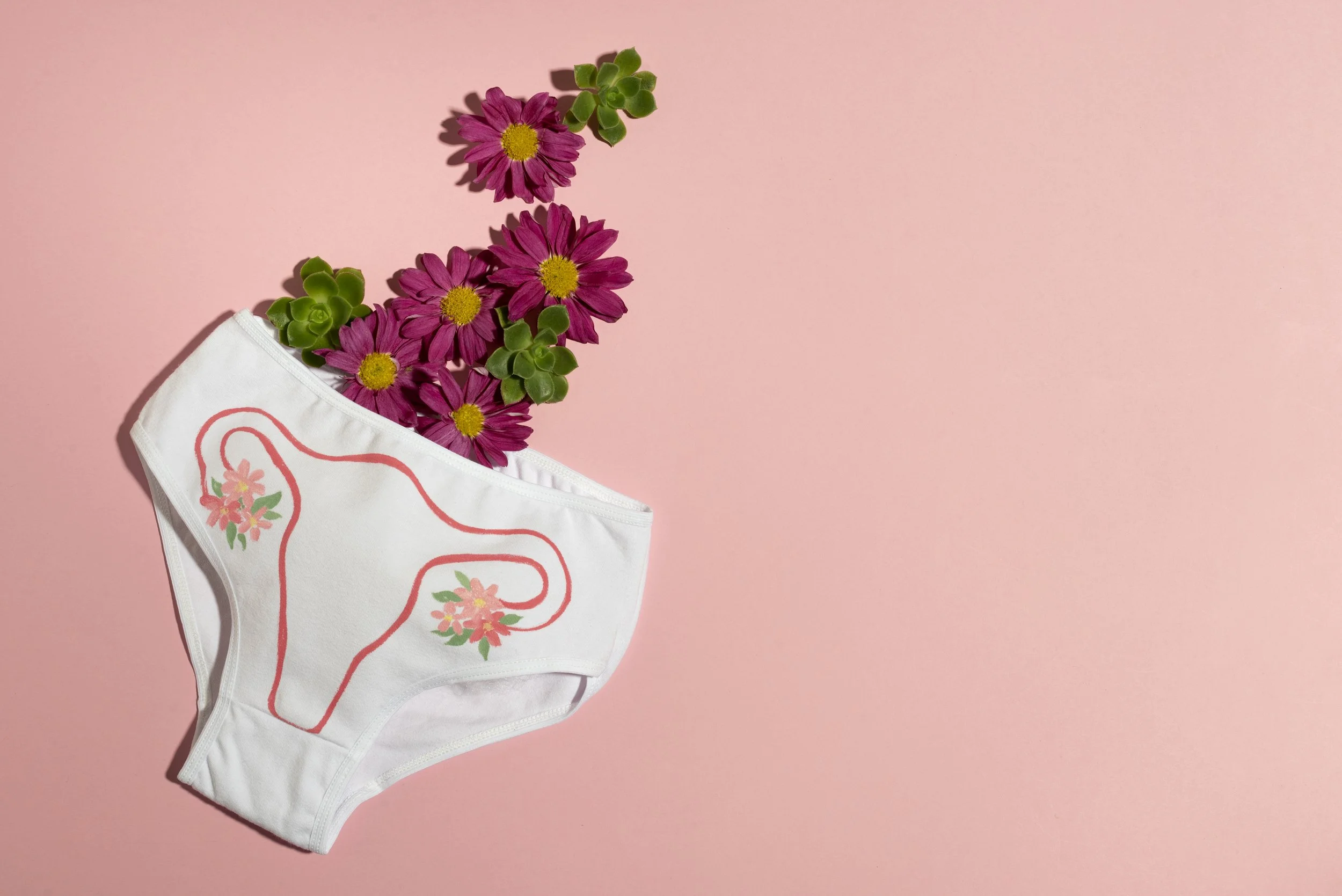 Pink flowers and green succulents emerging from a white face mask with a floral design on a pink background.