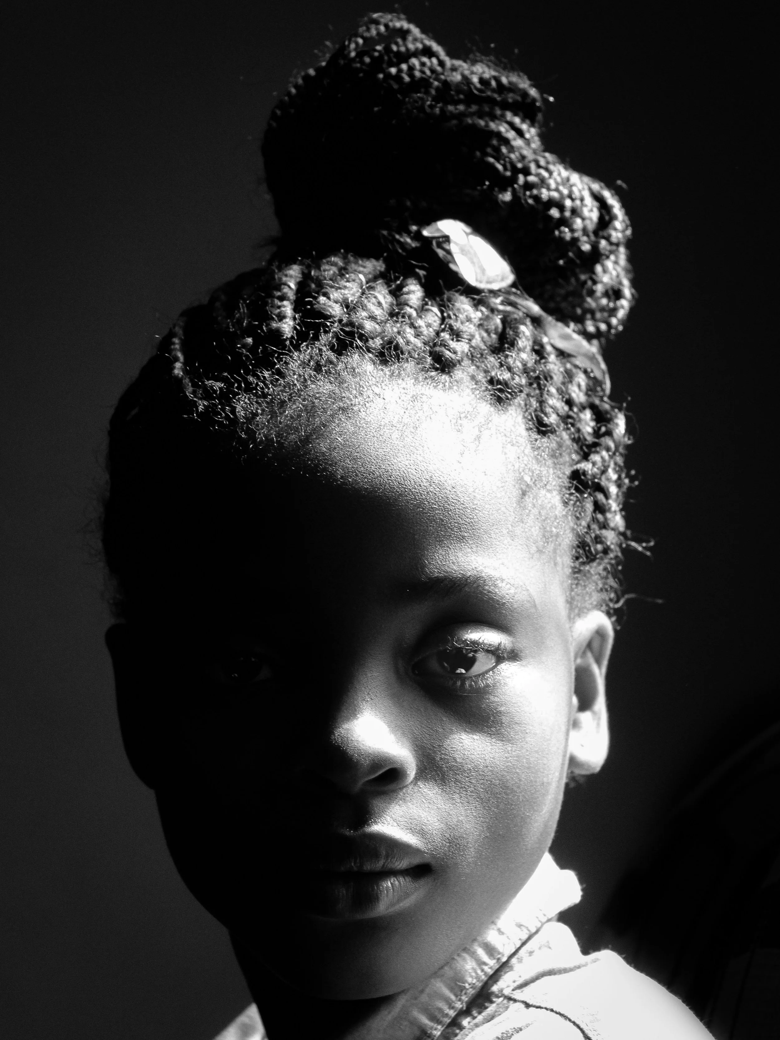 Black and white photograph of a person's face showing only the right half, with a focus on curly hair, eyebrow, eye, and lips, lit from the side creating shadows.