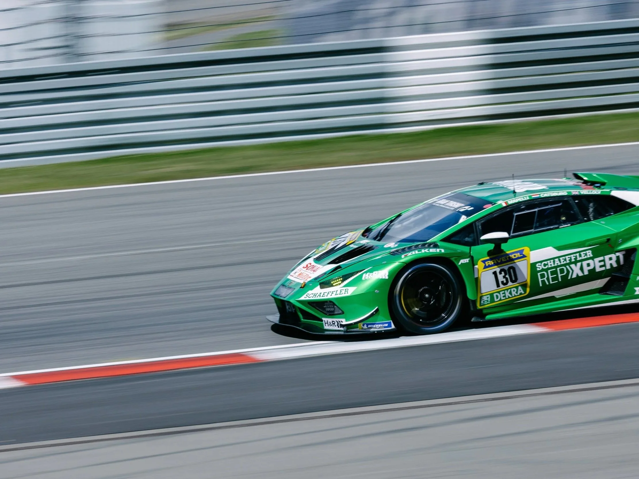 A green race car speeding on a race track with blurred background and tire marks.