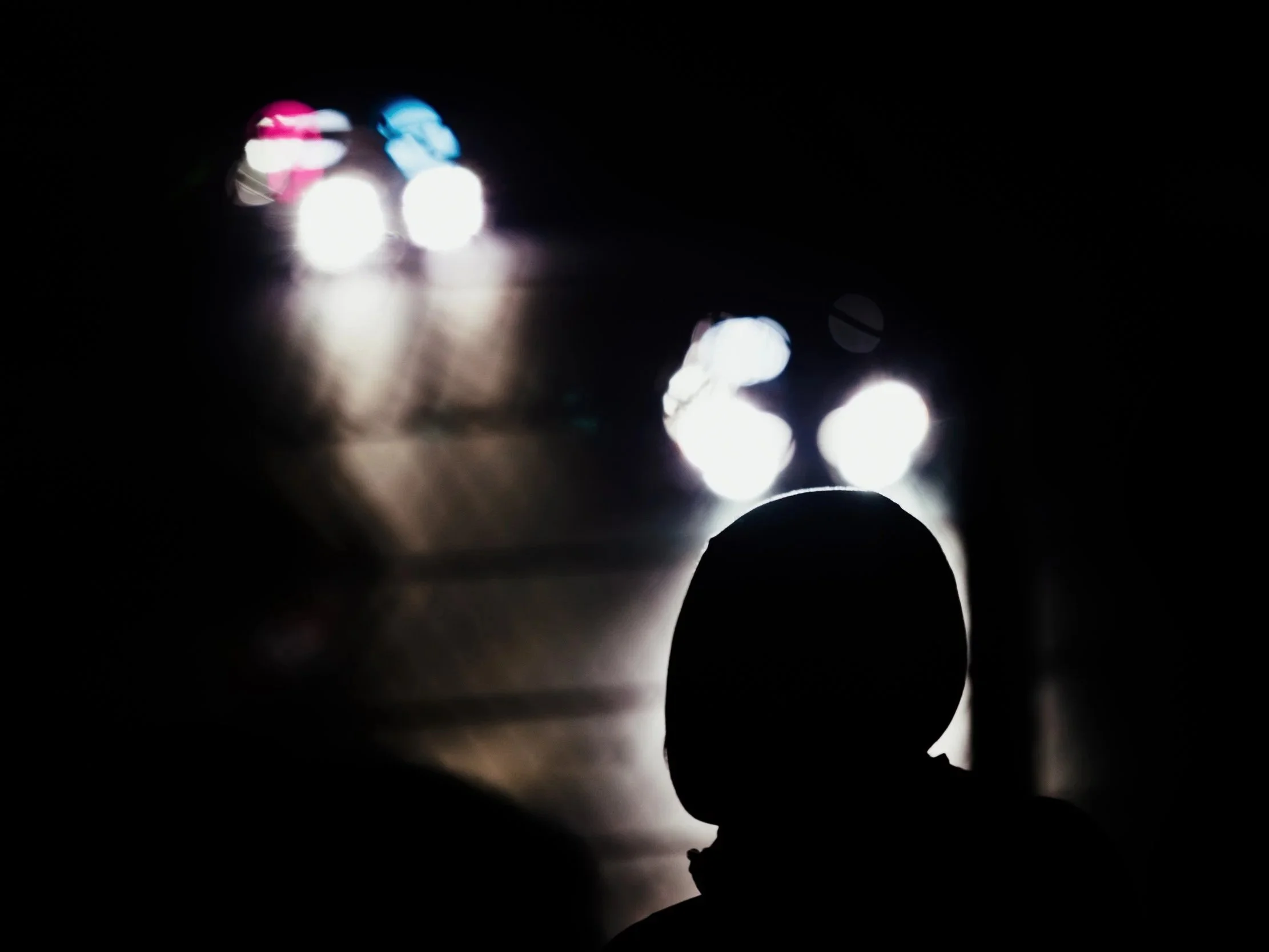A silhouette of a person is seen in front of bright lights reflecting on a dark surface, with the lights creating a bokeh effect in the background.