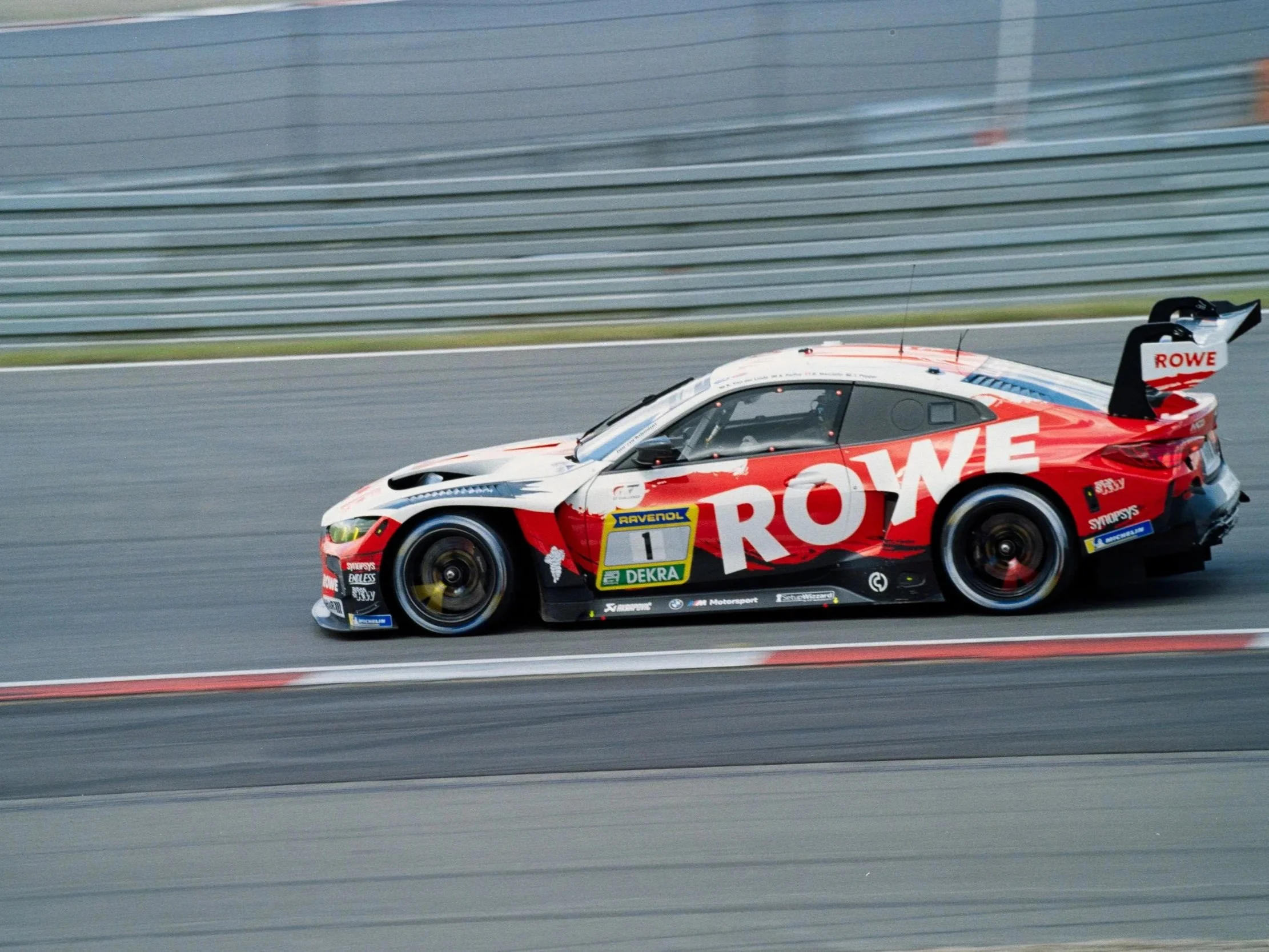 A race car on a track with motion blur in the background, displaying sponsorship logos including ROWE and Dewalt.