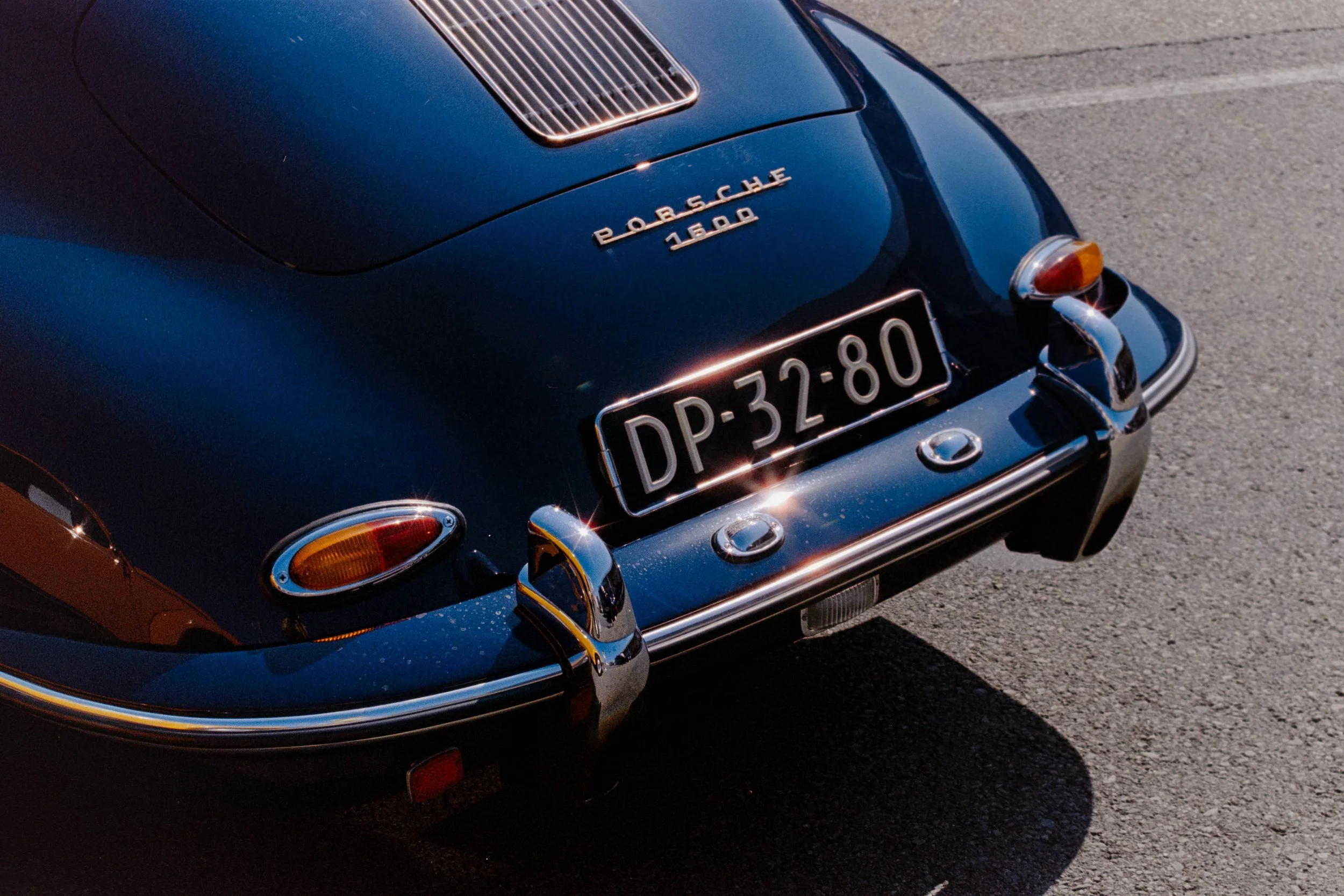 Close-up of a vintage black Porsche 1600 sports car's rear, showing the Porsche badge, rear lights, and license plate on a paved surface.