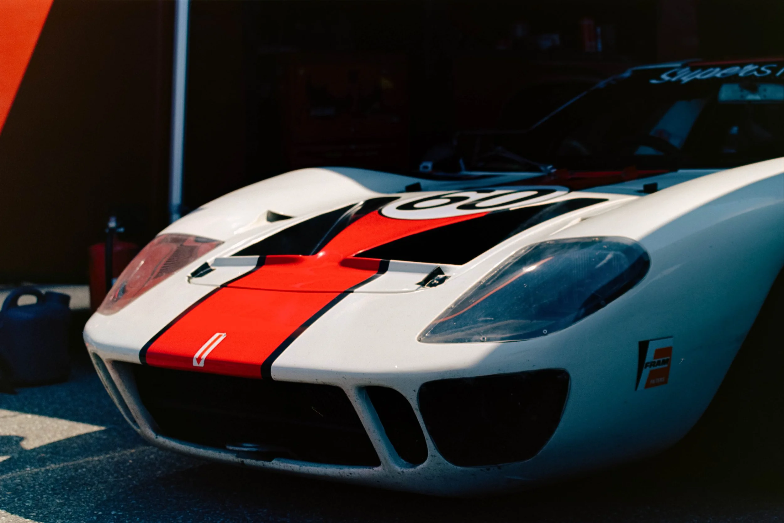 Close-up of a racing car with a white body and red and black stripes, featuring the number 20 on the hood, parked in a garage or service area.