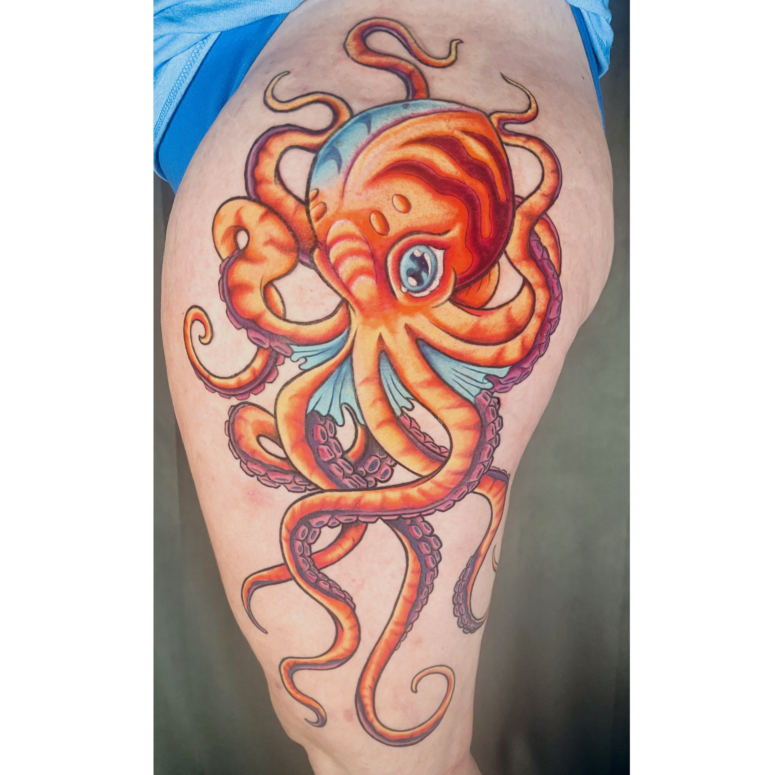 Colorful tattoo of a stylized octopus with shades of orange, red, purple, and blue on a person's upper arm.