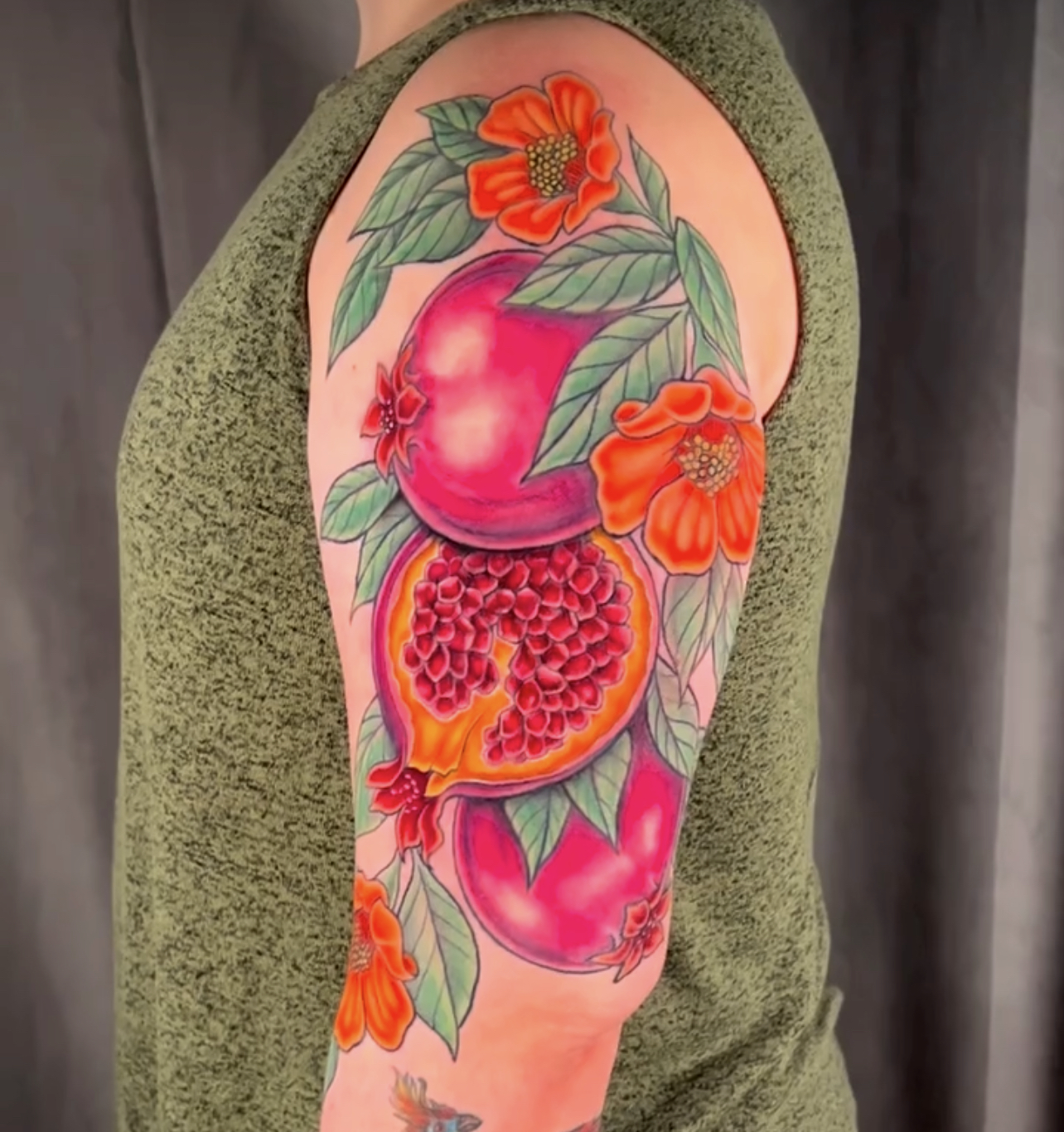 Colorful tattoo of pomegranate and flowers on person's upper arm.
