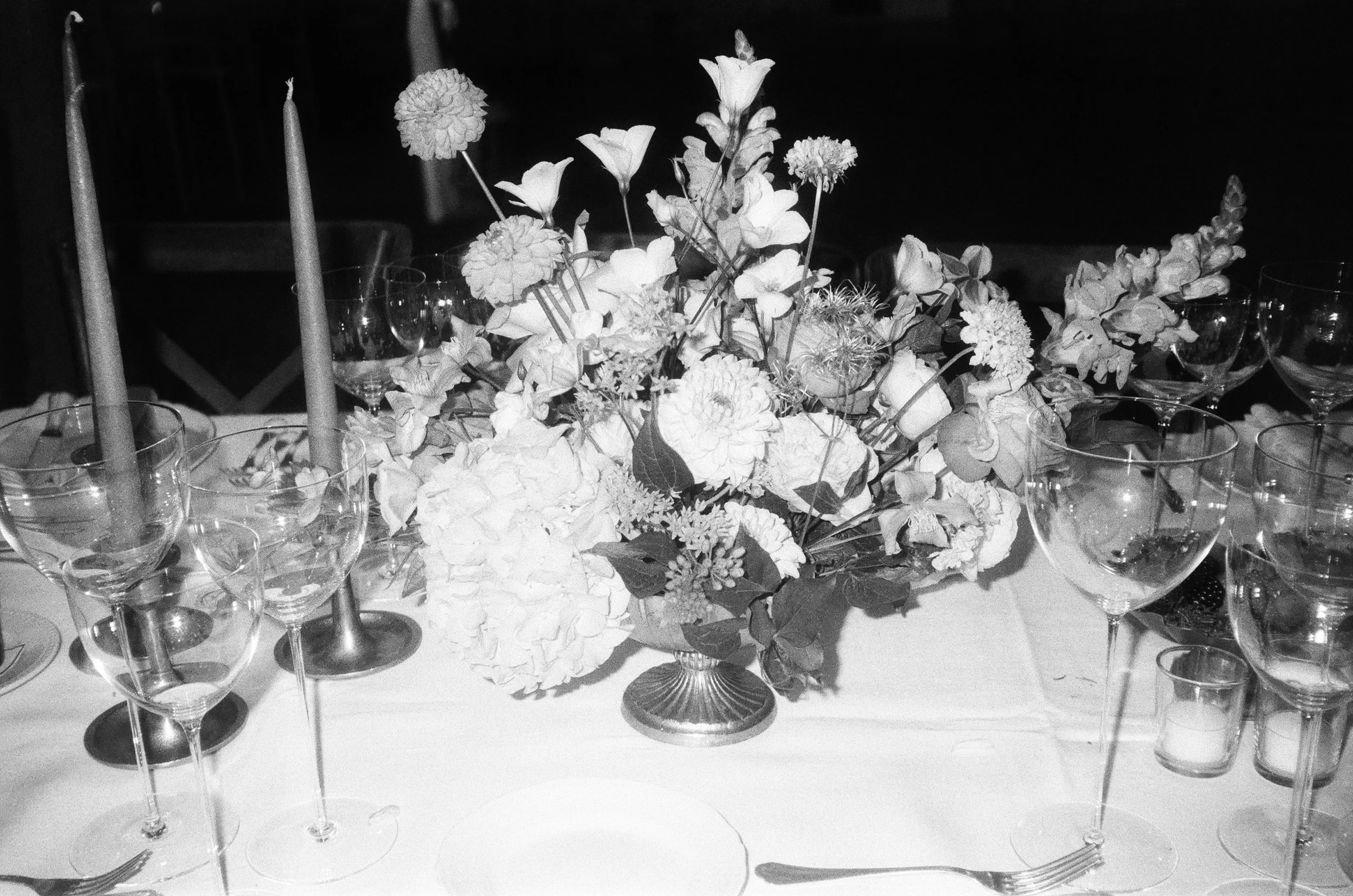 Un centro tavola con fiori e candele, circondato da bicchieri e posate su un tavolo elegante.