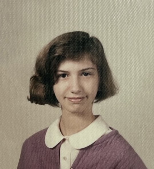 Ragazza con capelli corti, indossa una maglietta viola con collo bianco su uno sfondo beige.