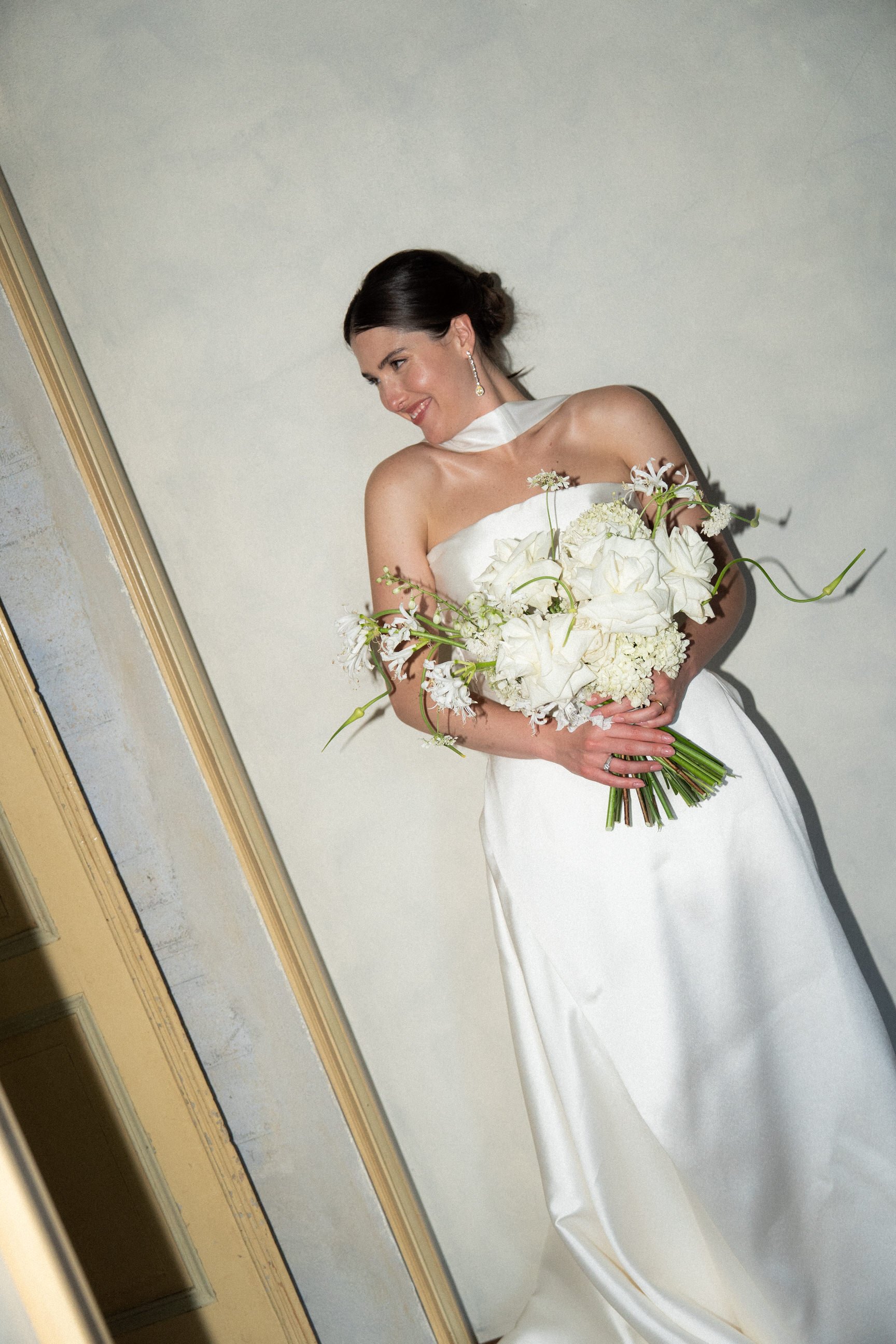 Una donna in abito bianco da sposa che sorride mentre tiene un grande bouquet di fiori bianchi.