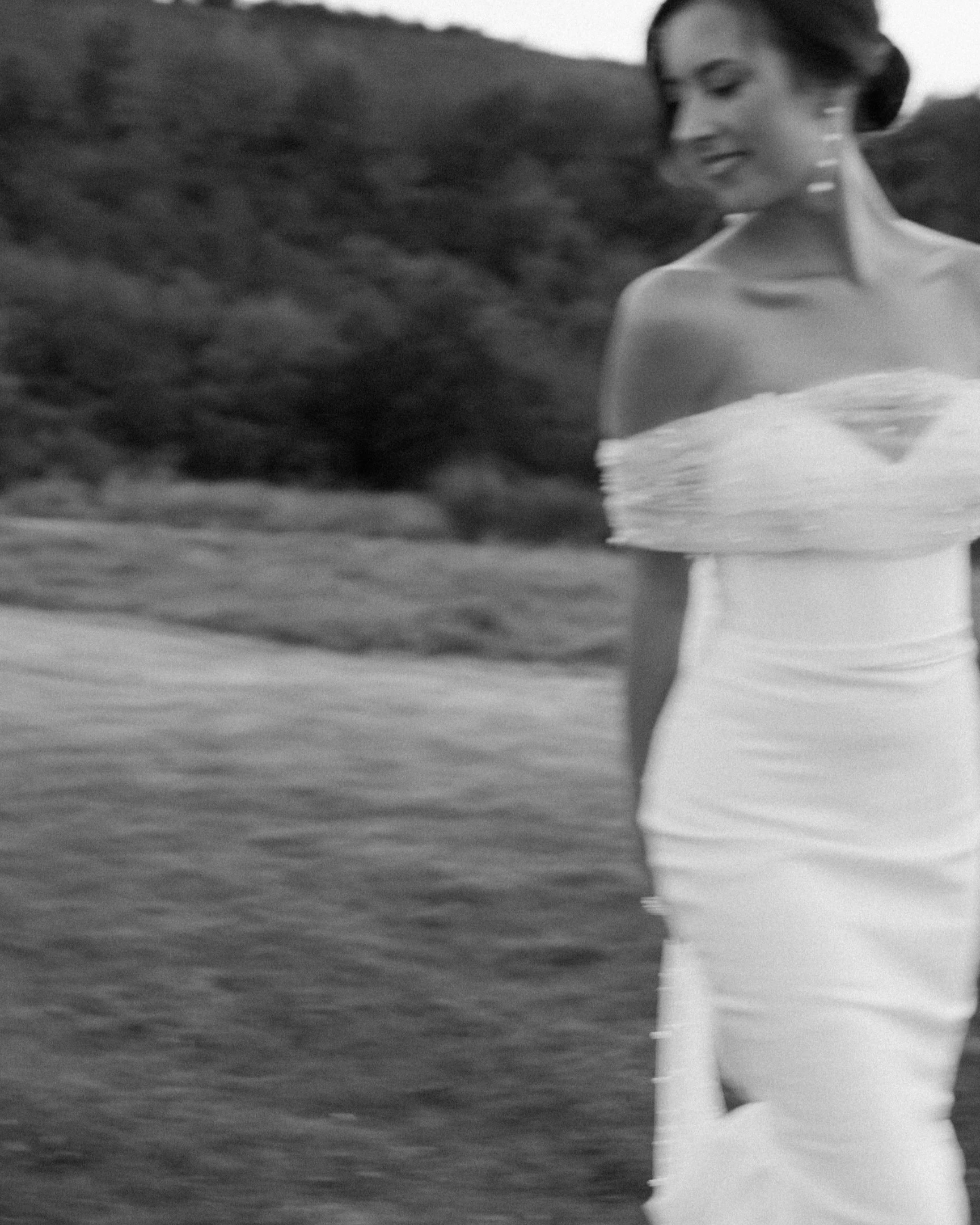Una donna in abito bianco sorride mentre cammina, con lo sfondo di una natura verde e alberi.