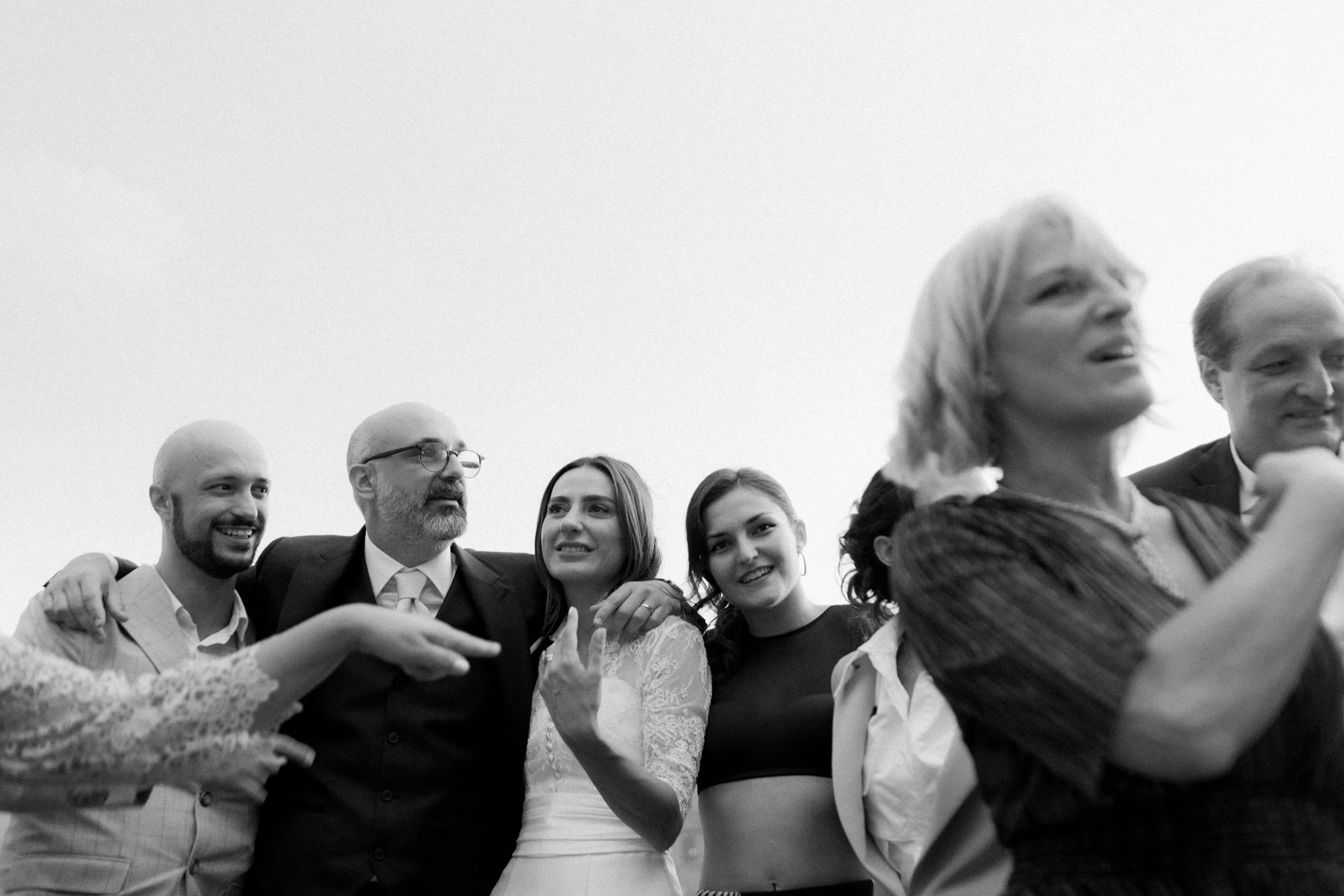 Un gruppo di persone sorridenti e felici si abbracciano e si tengono per mano, indossando abiti eleganti, in un'occasione di festa o celebrazione.