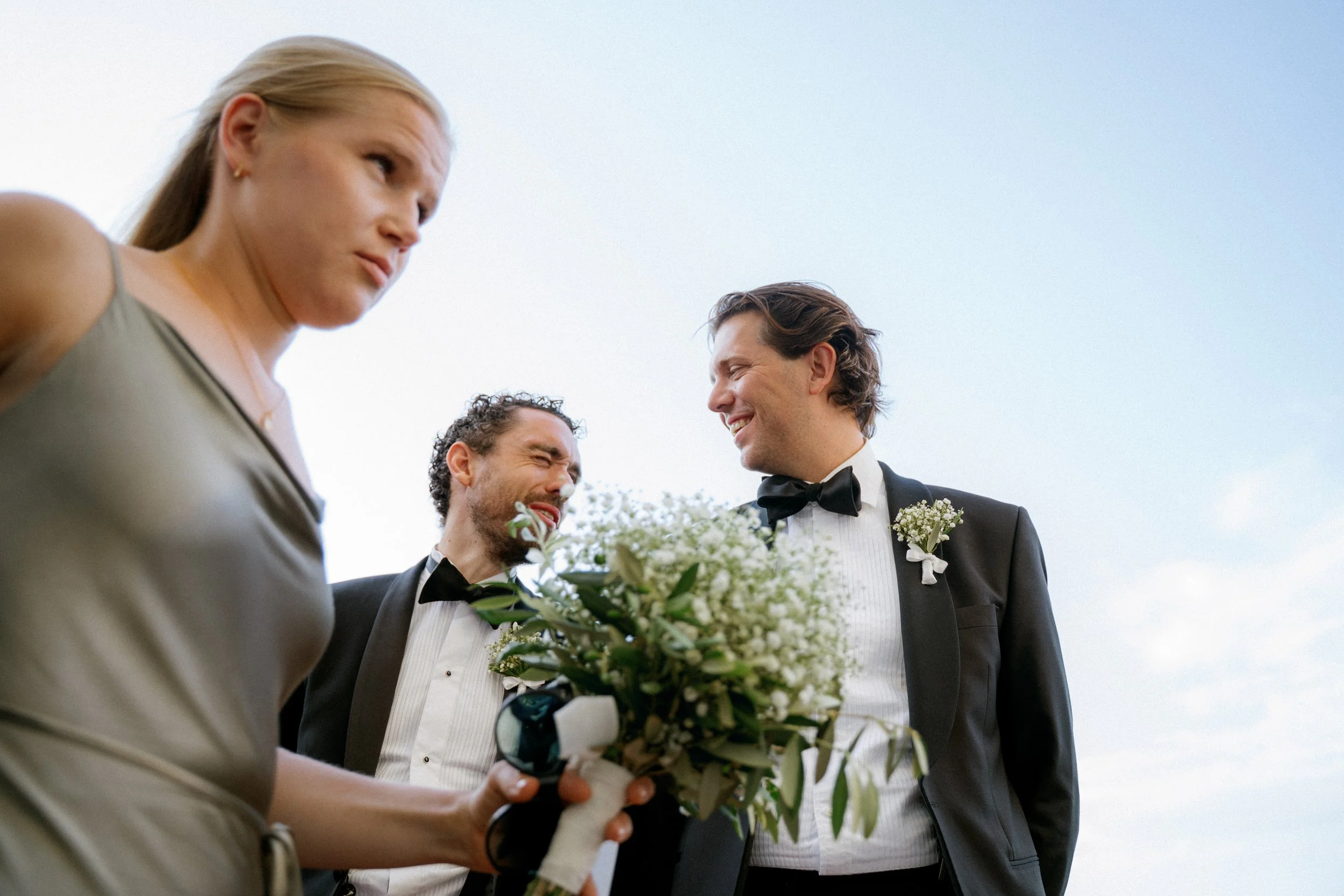 Sposa e sposo sorridenti in abiti eleganti durante il matrimonio all'aperto, condividono un momento di gioia con altri partecipanti.