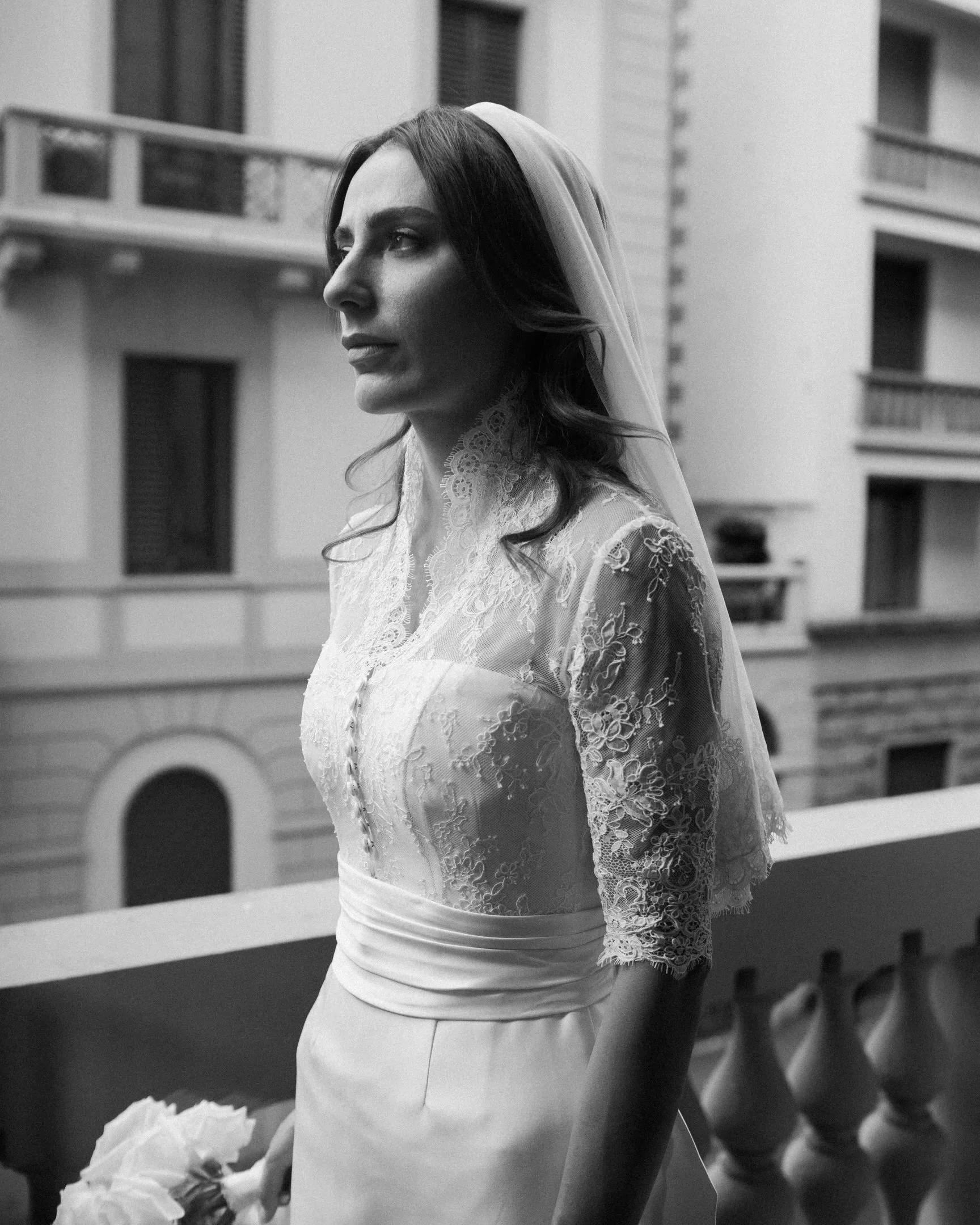 Una donna in abito bianco con un velo sulla testa, scattata in un contesto urbano, in bianco e nero.