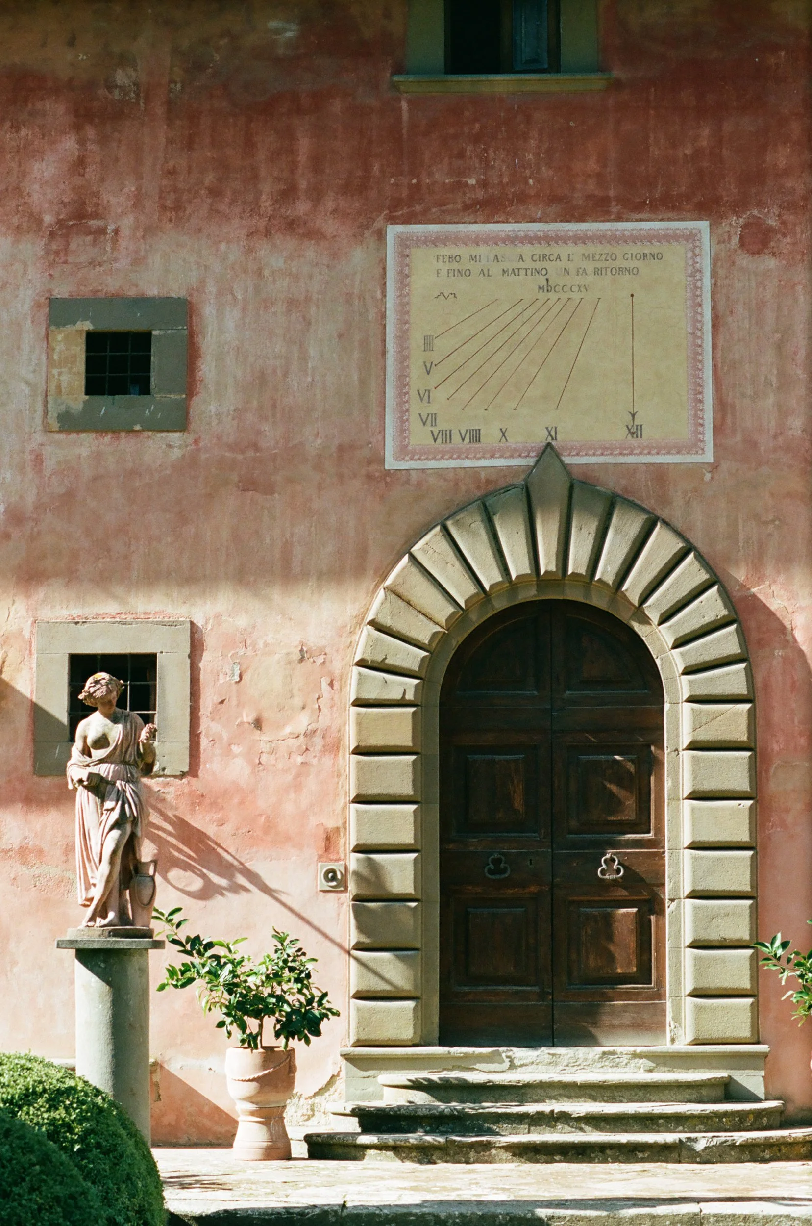 Facciata antico edificio con portale in pietra, statue di donna in statua, piante e finestre in alto, orologio solare con scritte in italiano