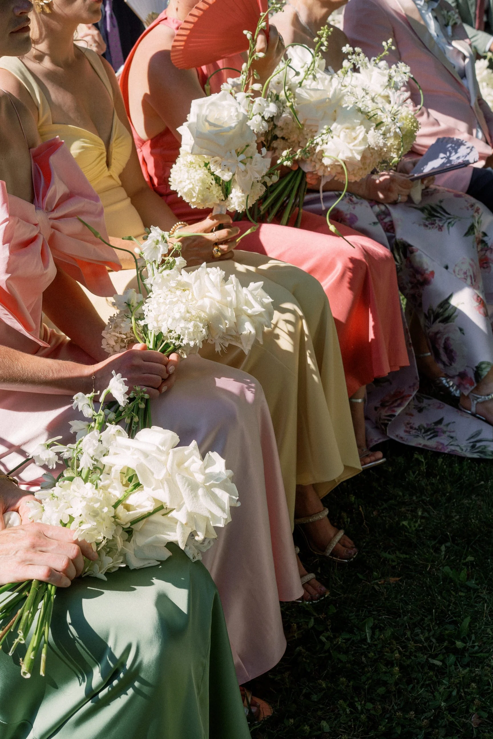 Persone sedute ai matrimoni con abiti eleganti colorati e bouquet di fiori bianchi.