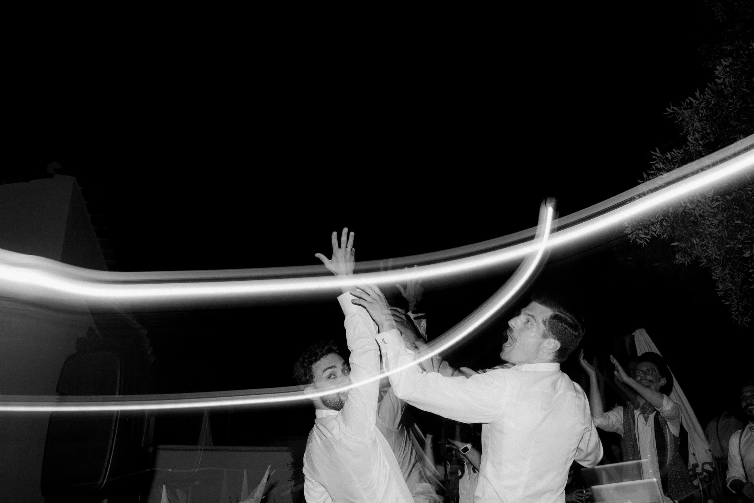 Persone in festa con luci di movimento e uno dei partecipanti al centro che sorride e alza la mano