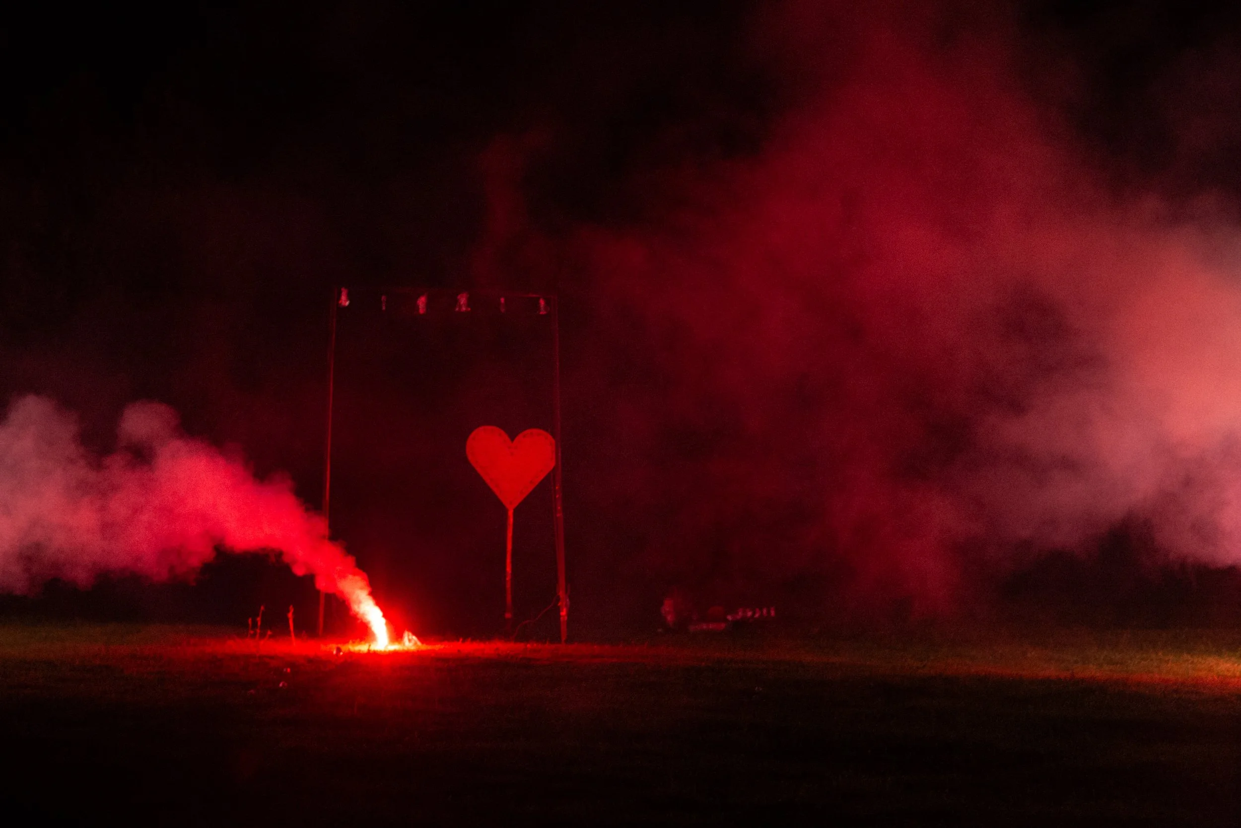 Cuore luminoso rosso nel cielo notturno, circondato da fumo rosso e luci rosse.