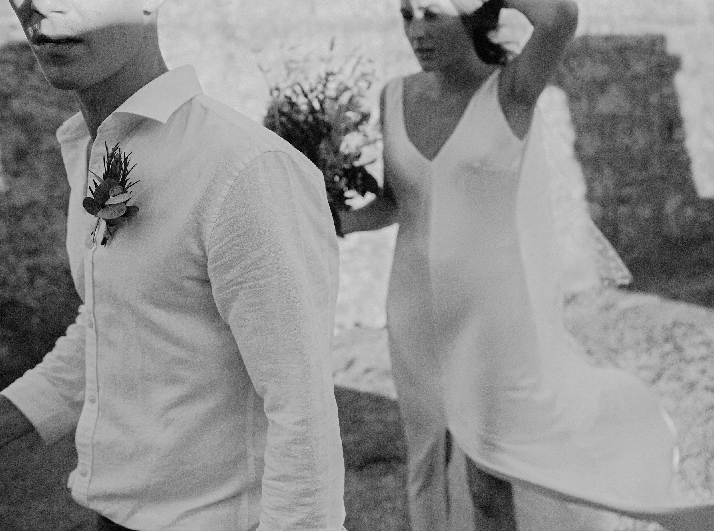 Due donne vestite in bianco, una con camicia e l'altra con top, camminano su una strada di campagna con alberi e pareti in pietra.