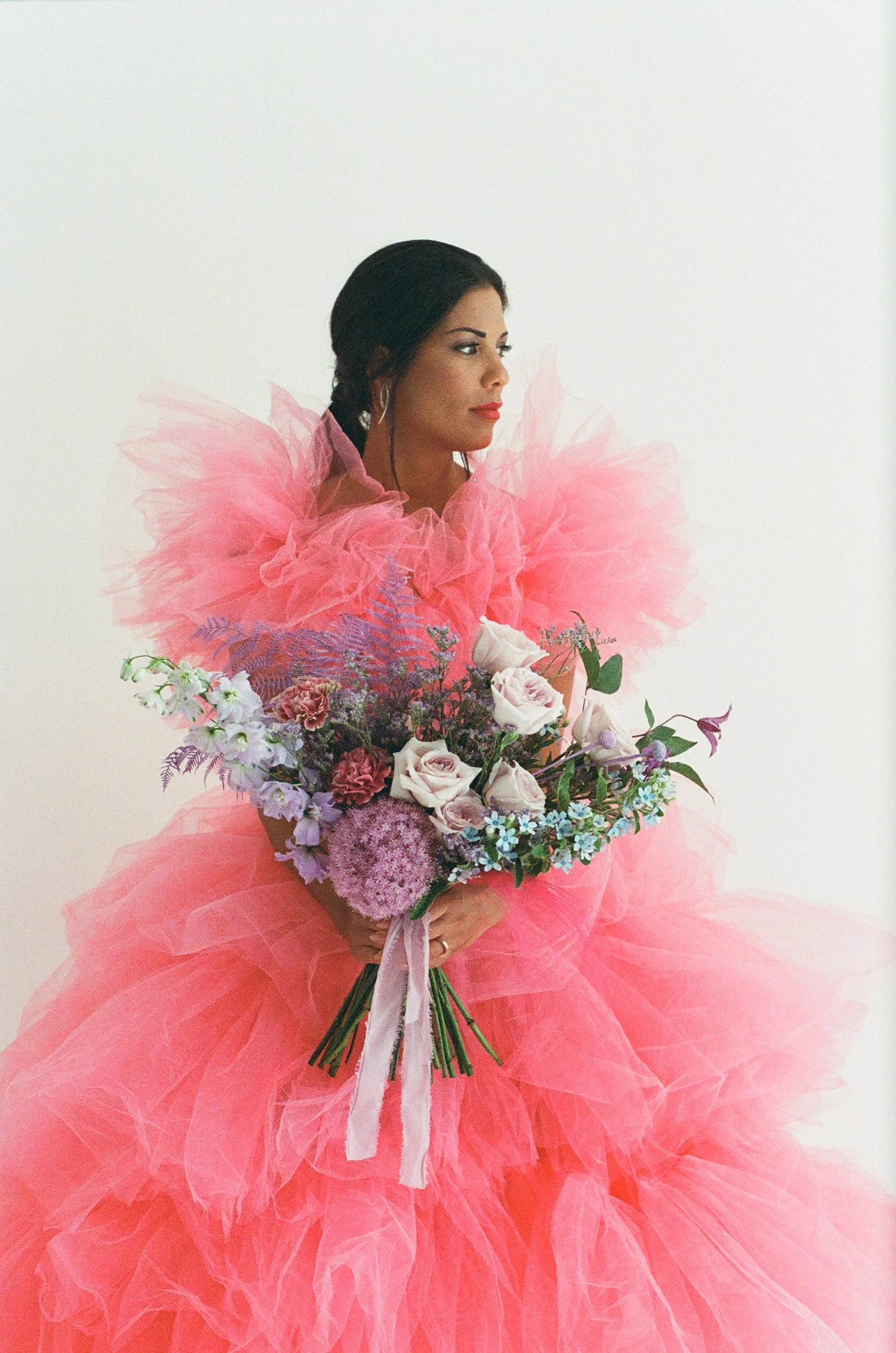 Una donna indossa un abito lungo di tulle rosa e tiene un grande mazzo di fiori misti.
