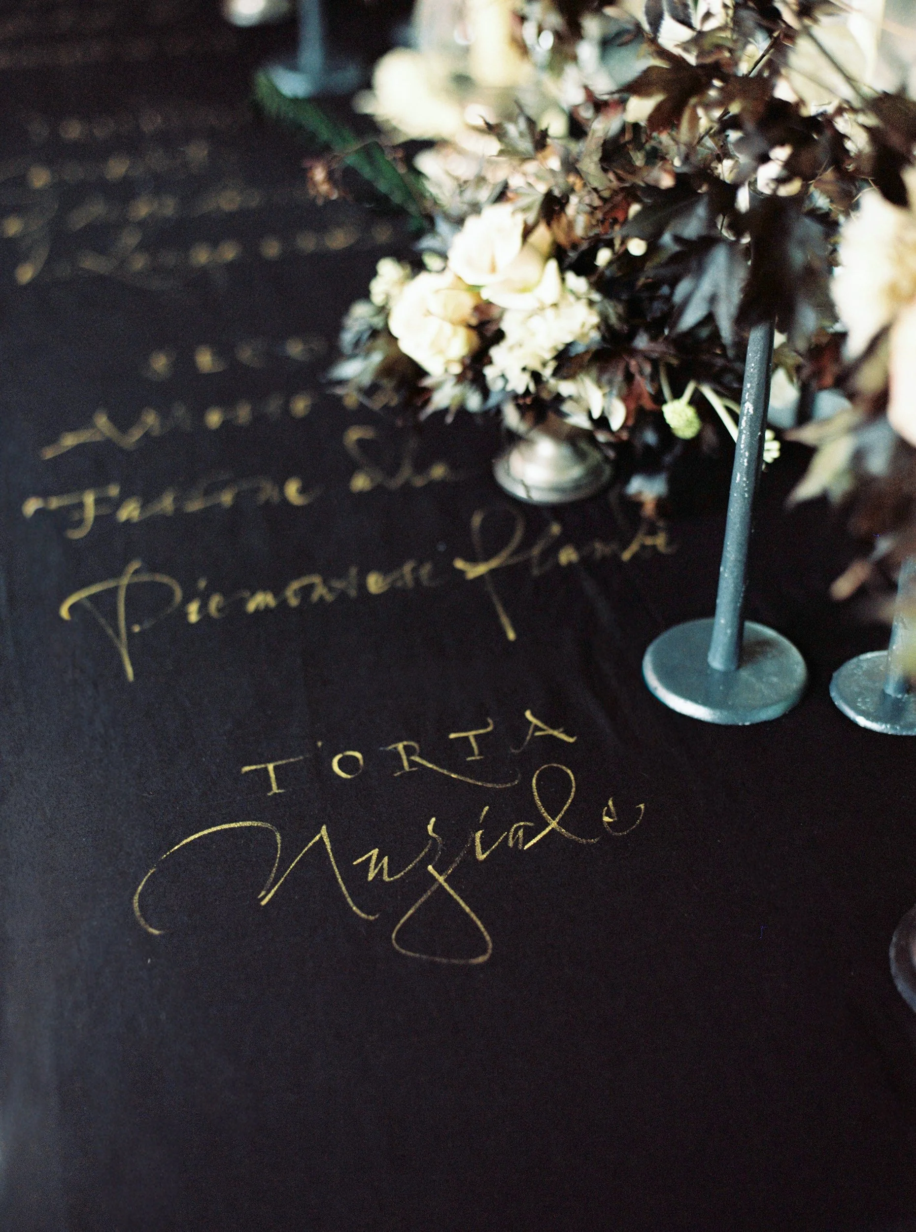Fiori bianchi decorano un tavolo nero con scritte dorate. Due candeline blu scuro sono poste in piedi accanto ai fiori.