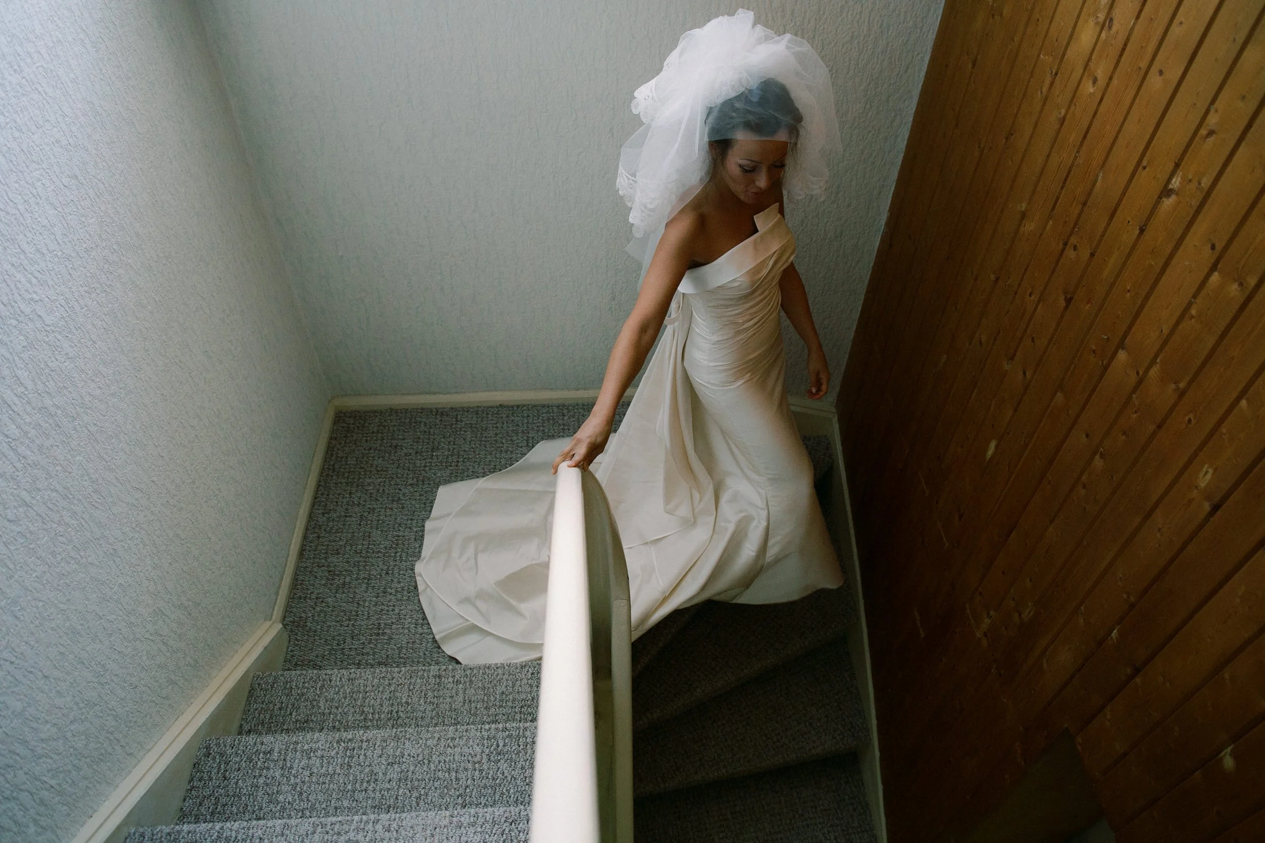 Una donna in abito da sposa cammina su una scala stretta vicino a una parete di legno.