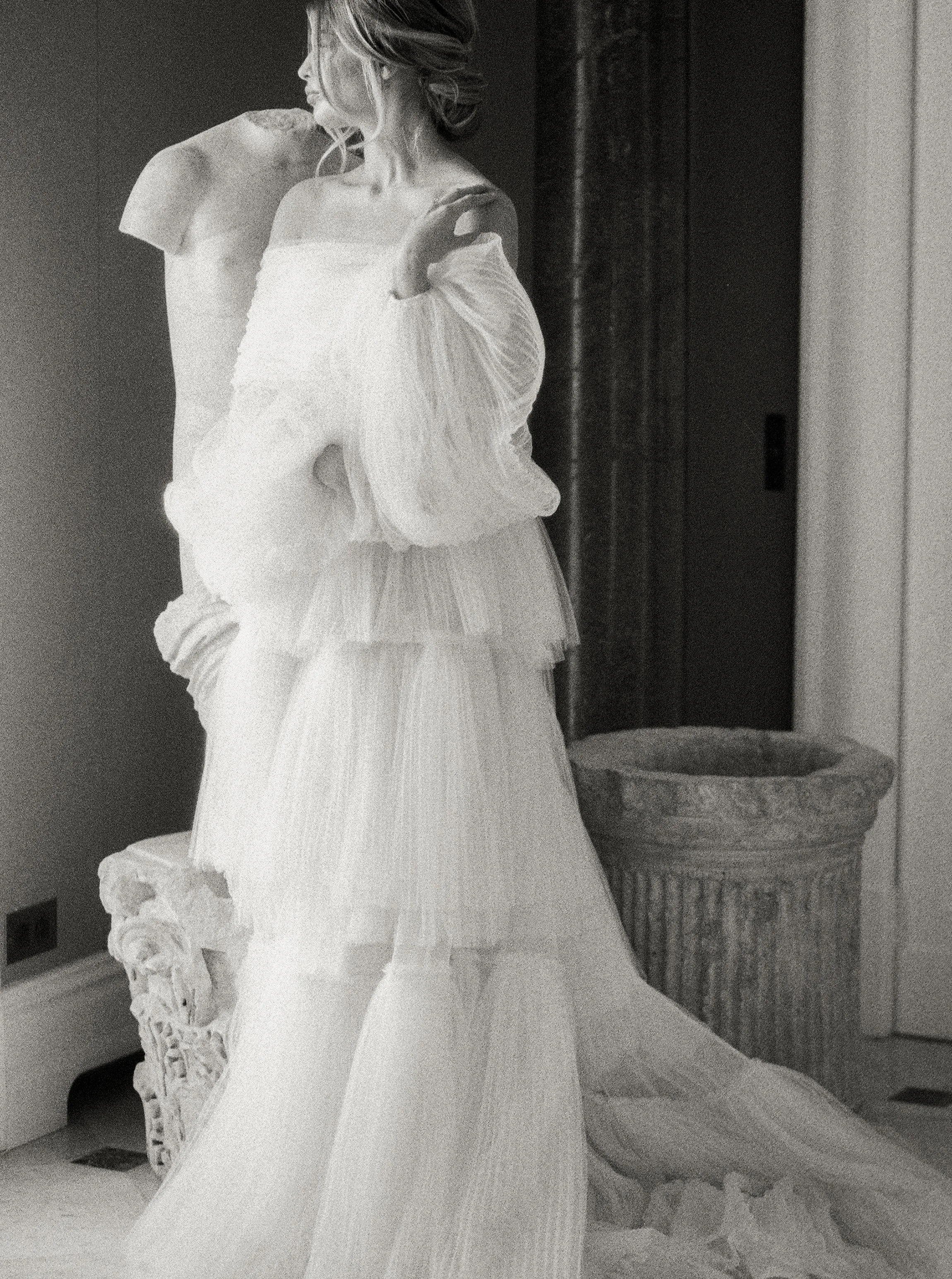 Statua di una donna con un vestito lungo, in stile classico, posizionata accanto a una colonna decorativa in un ambiente interno.