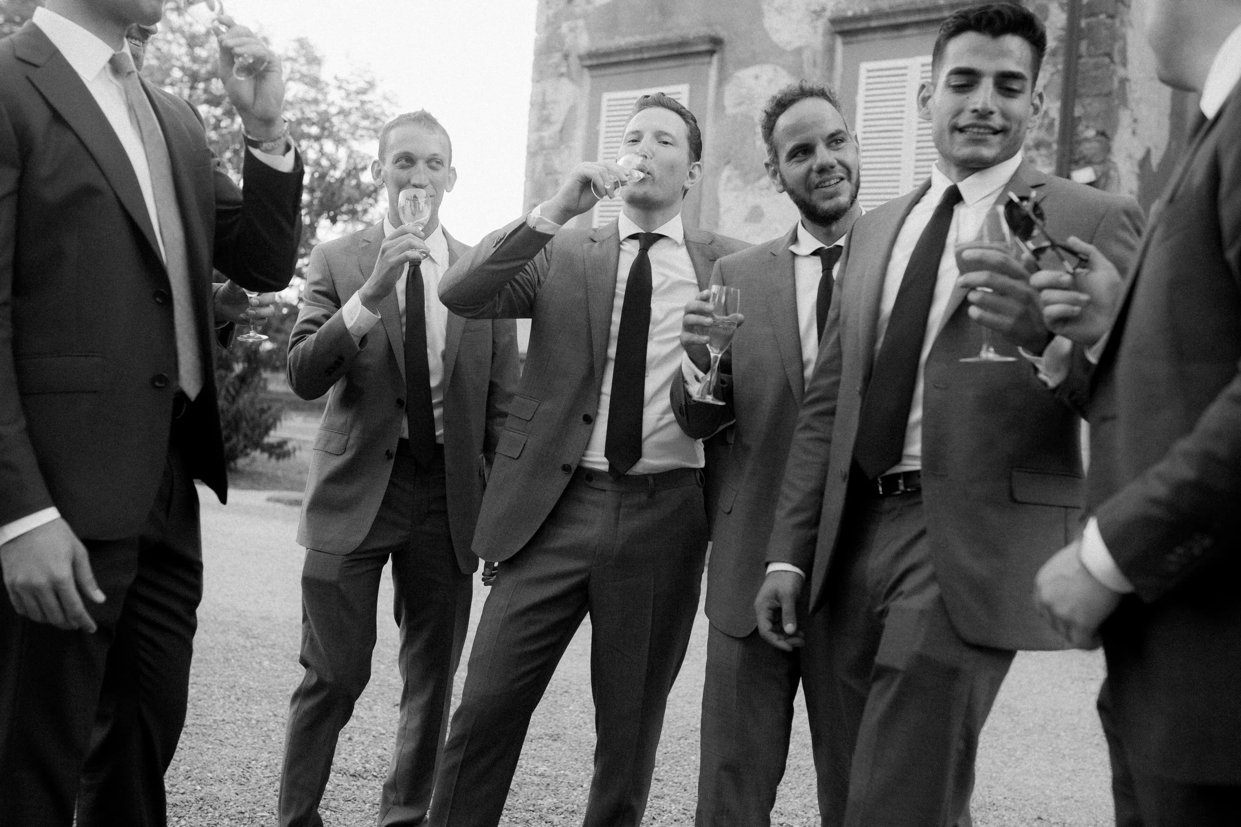Gruppo di uomini in abiti eleganti che brindano con calici di vino o champagne all'aperto.