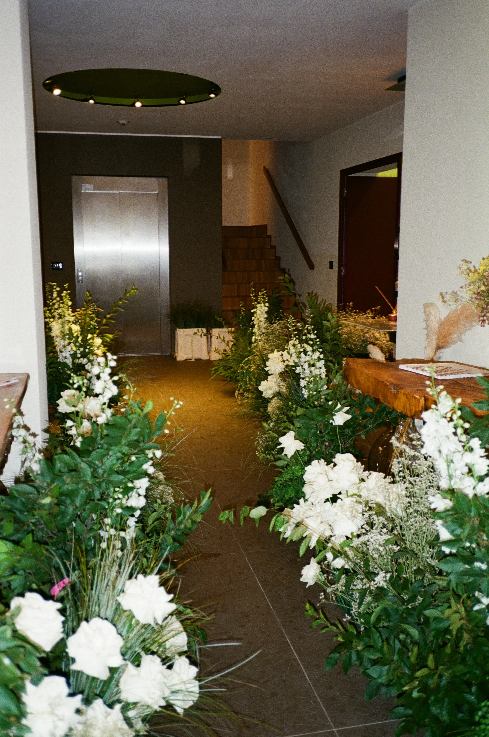 Ingresso di un edificio con decorazioni floreali, ascensore e scale di legno.