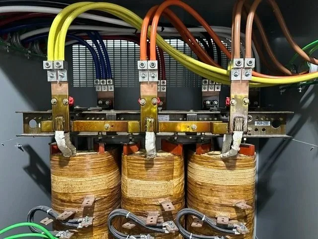 Close-up of electrical components inside a control panel, including three large copper coils, wiring, and terminal connections.