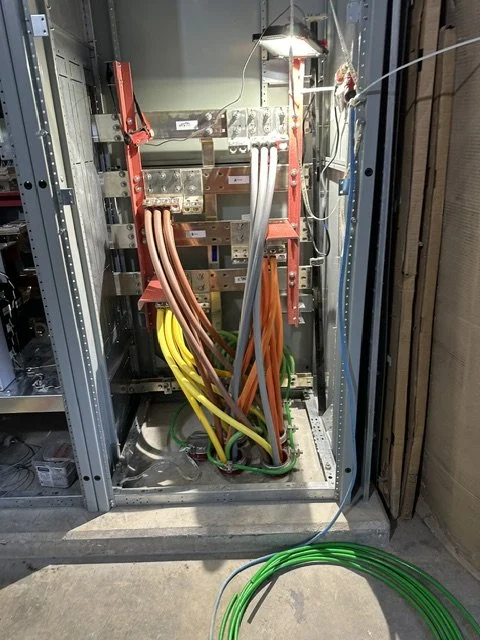 Electrical cabinet with colorful wires and components, partially open door, green wire coil on the ground.