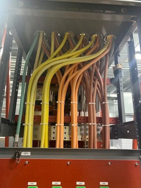 Electrical switchgear with multiple colored power cables connected to bus bars inside an industrial panel.