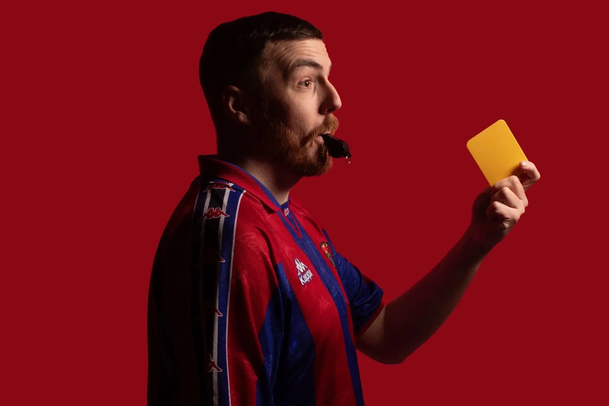 A man in a sports jersey holding a yellow card, with a red background.