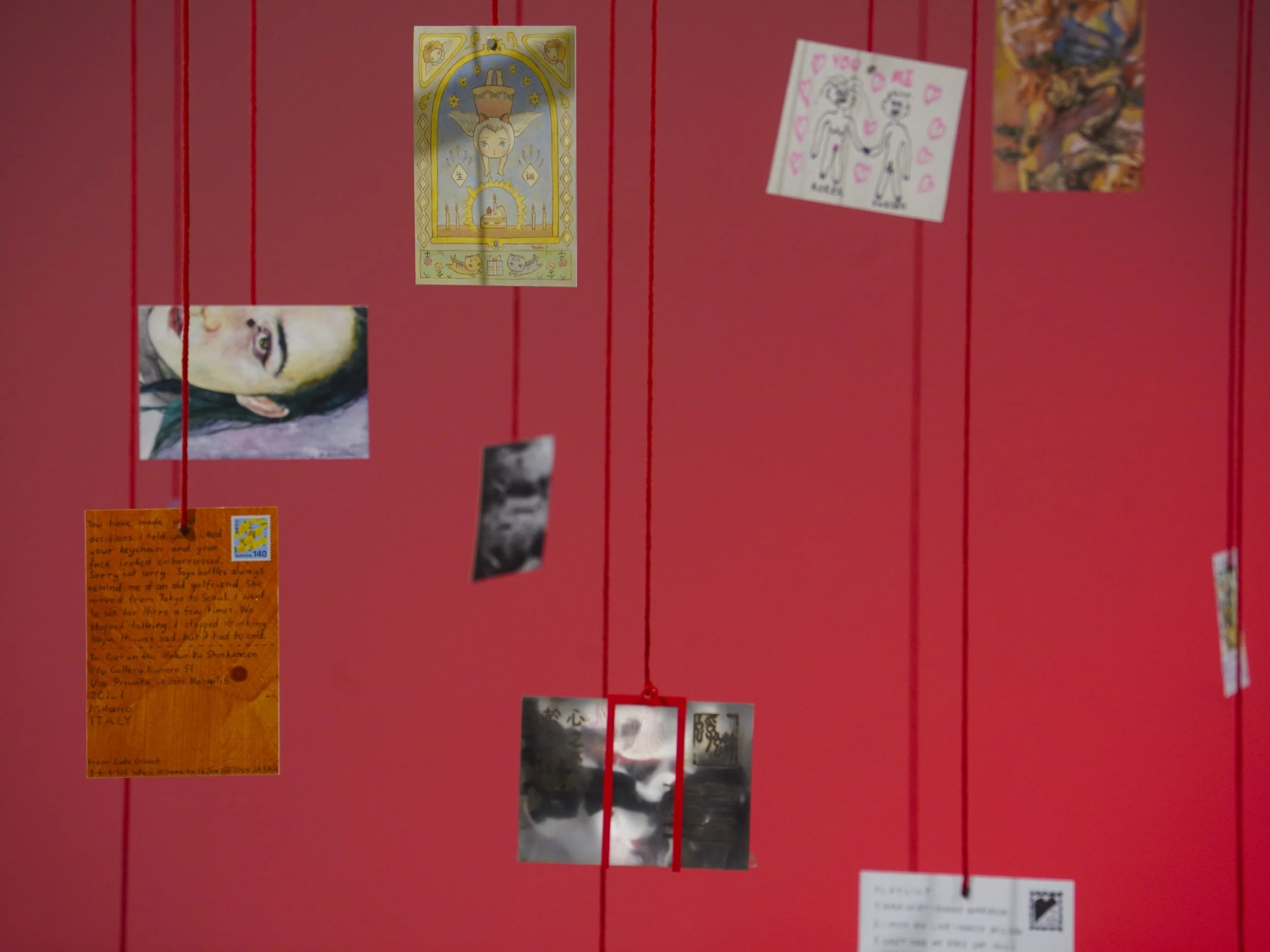 Red wall decorated with various postcards, drawings, and photos hanging on red strings.