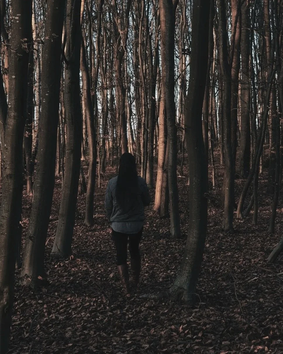 Frau geht durch Baumstämme im Wald hindurch