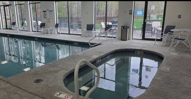 Indoor swimming pool and hot tub area with lounge chairs and large windows.