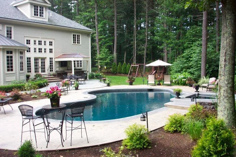 Backyard with swimming pool, patio furniture, playground set, and house surrounded by trees and garden.