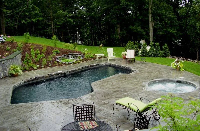 Backyard with a swimming pool and hot tub, surrounded by patio furniture and lush greenery.