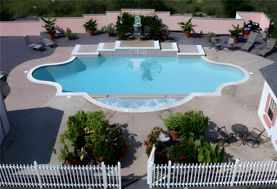 A backyard with a swimming pool, lounge chairs, and outdoor seating areas, surrounded by a white fence and landscaping.
