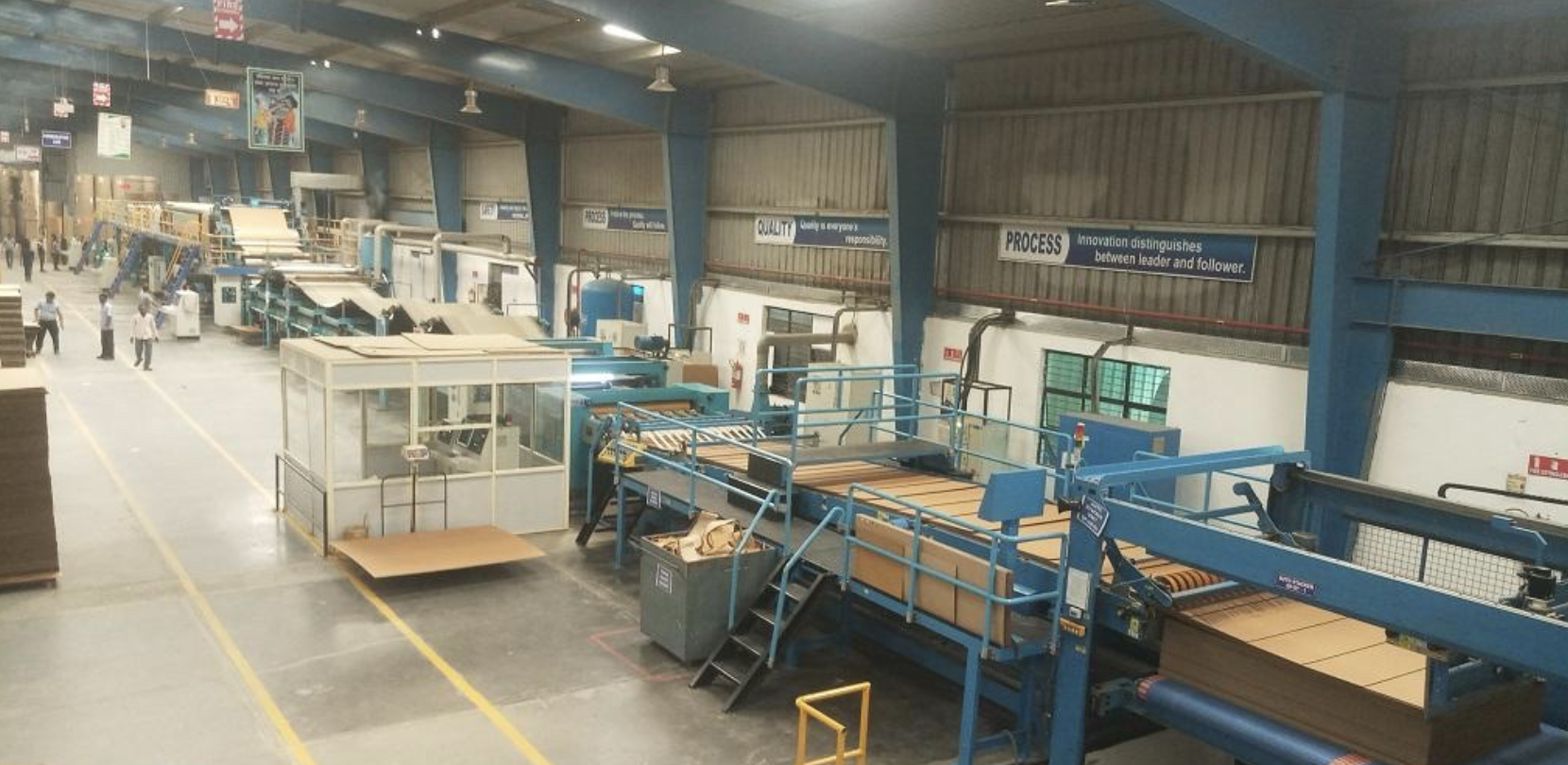 Industrial factory with machinery, workers, and conveyor belts in a spacious warehouse.