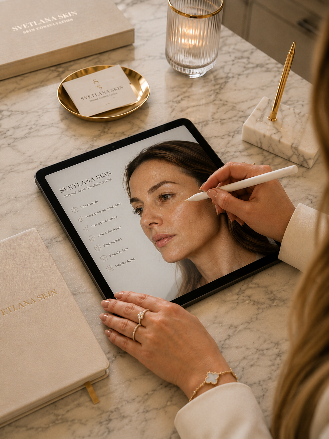 A woman is sitting at a marble table while using a tablet to consult an online skin care service called Svetlana Skin. She is gently touching her face with a stylus. The table has various items including a beige notebook, a small gold dish with skincare product cards, a lit candle, and a marble pen holder with a gold pen. The woman's hand is adorned with rings and a bracelet.